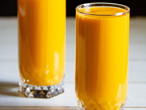 mango milkshake in two tall glasses on white table with a black background