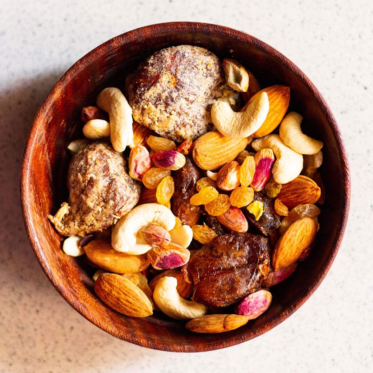 various nuts and dry fruits in a woodern bowl on a marble surface