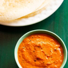 onion chutney in a green bowl with dosa stacked on a white plate on a dark green board