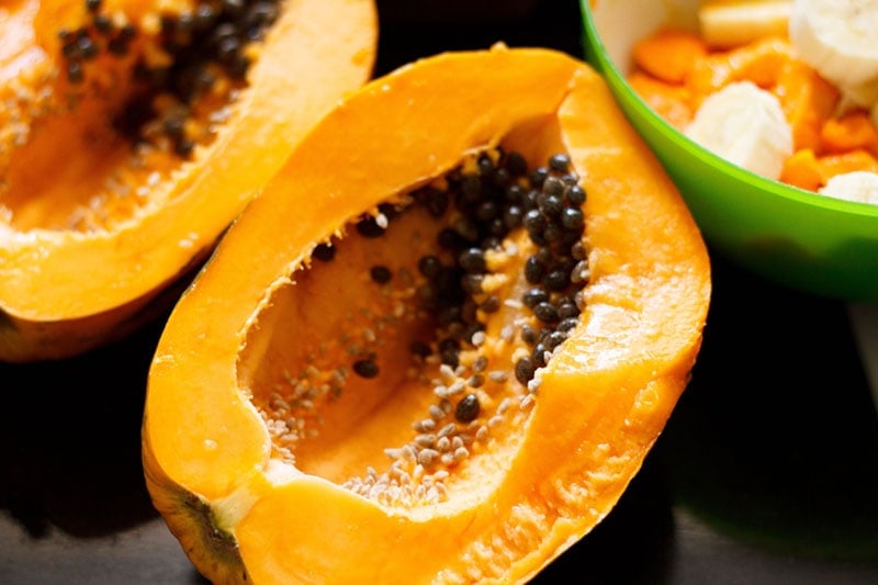 halved papaya with a green bowl with chopped mangoes, bananas at the top side