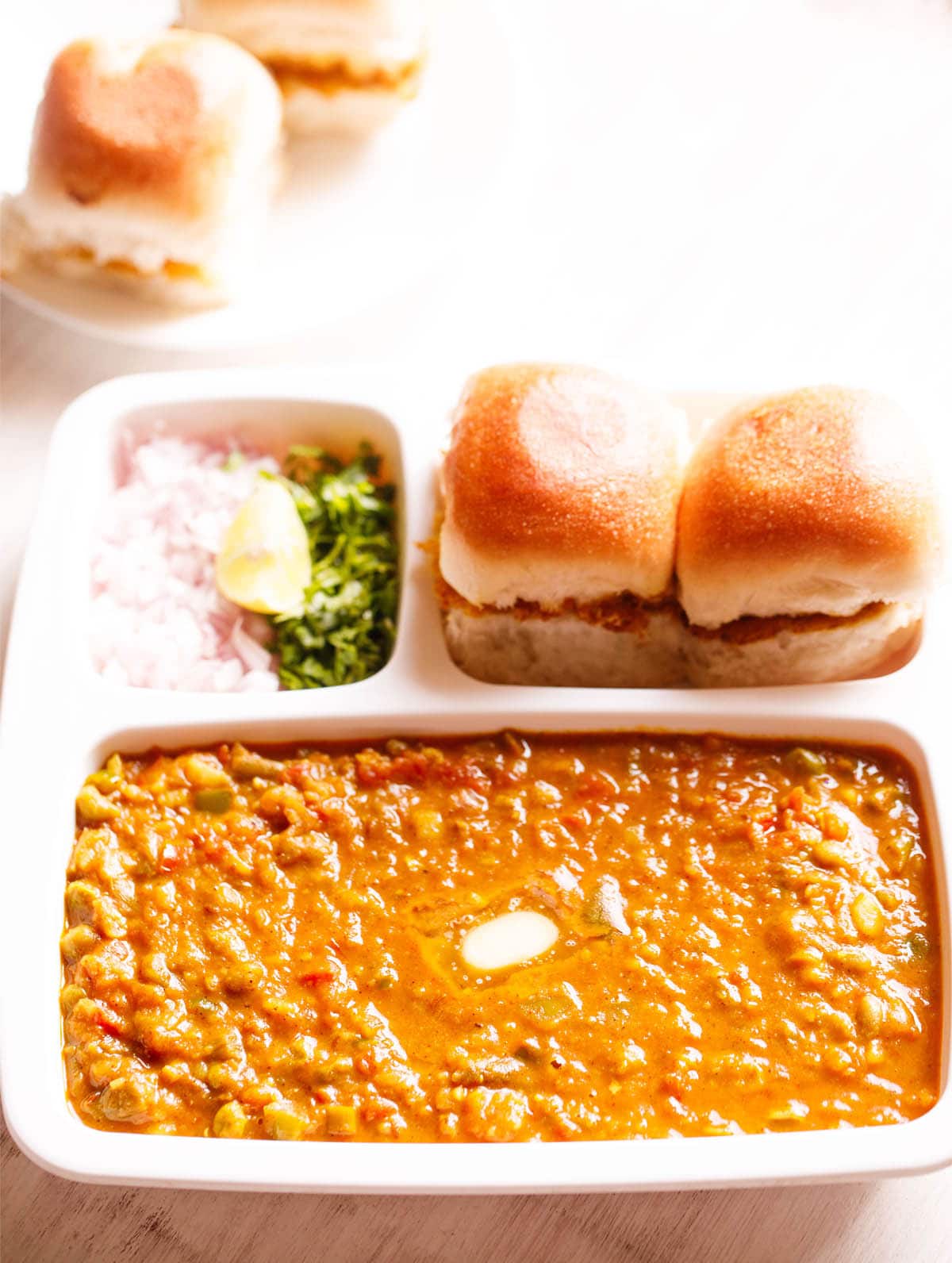 pav bhaji served in a rectangular serving tray with buttered pav and chopped onions, cilantro and lemon wedges