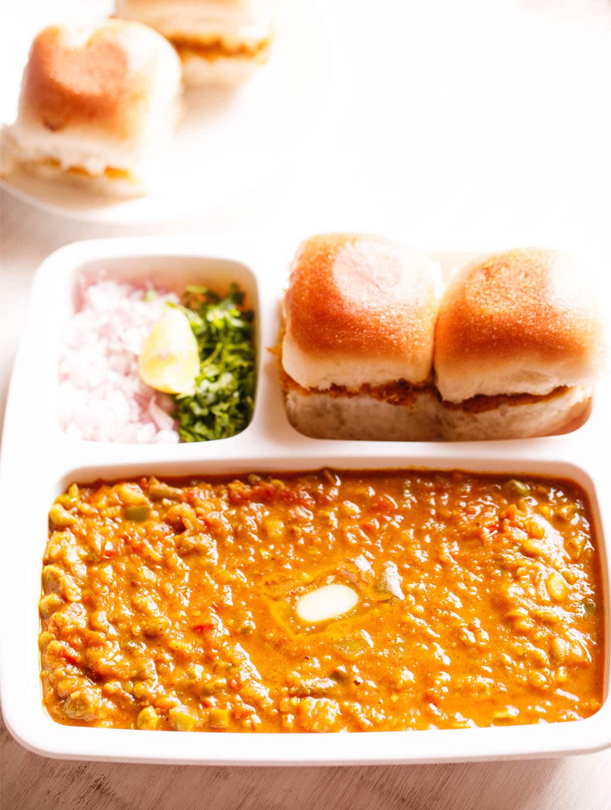 pav bhaji tarjoillaan suorakulmaisessa tarjoilualustassa voitetulla pavillä ja hienonnetulla sipulilla, korianterilla ja sitruunakiiloilla