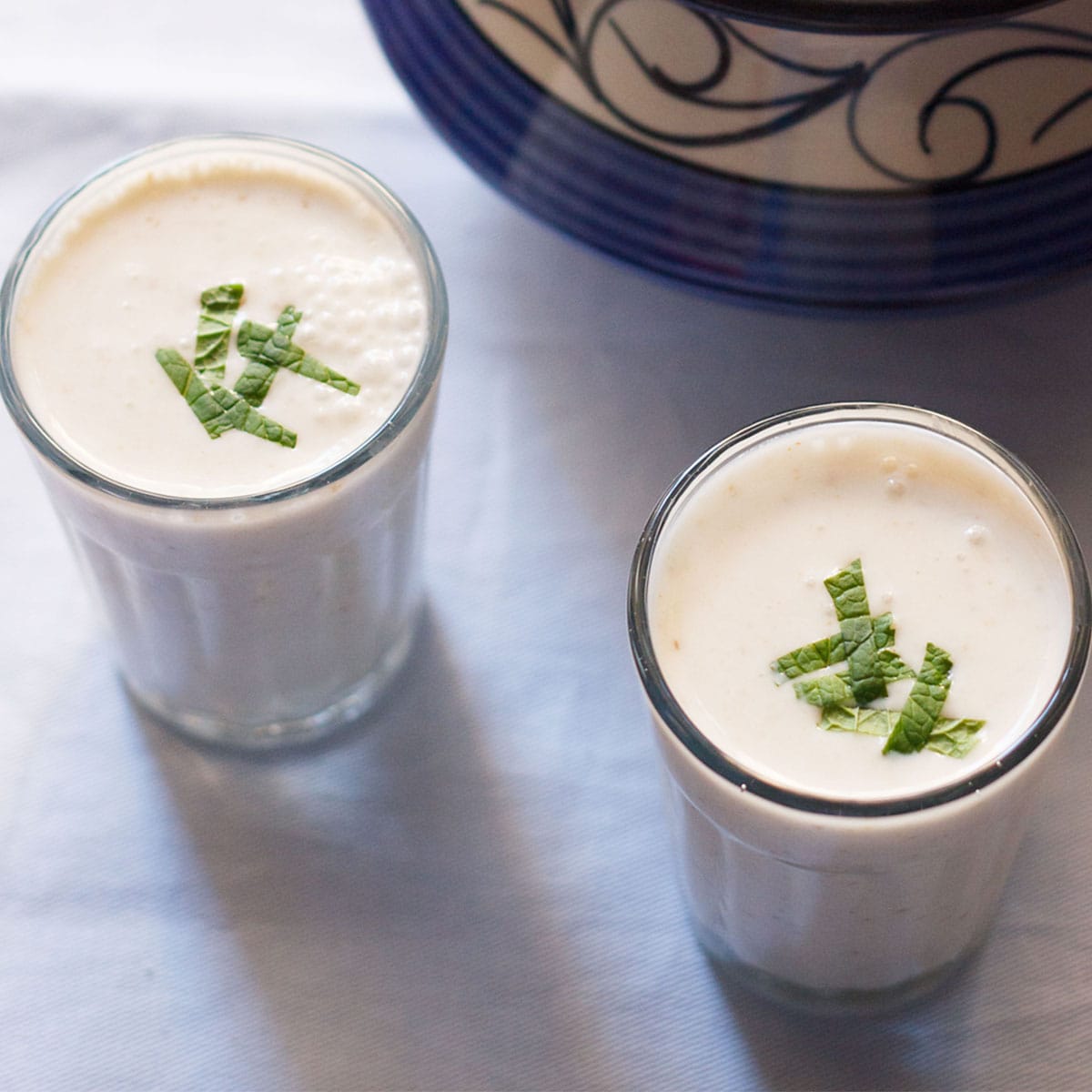 salted lassi served in two small glasses on a light blue linen lined on top of a small table