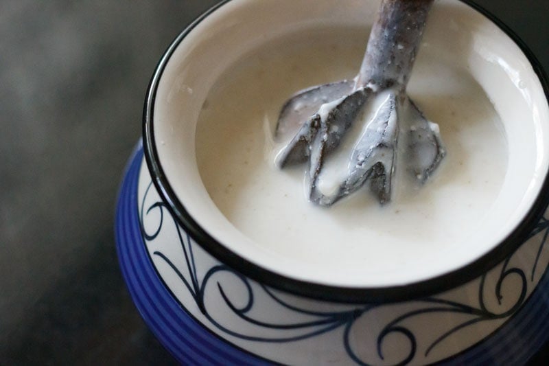 yogurt, water, seasonings being blended with a hand wooden churner to make salted lassi