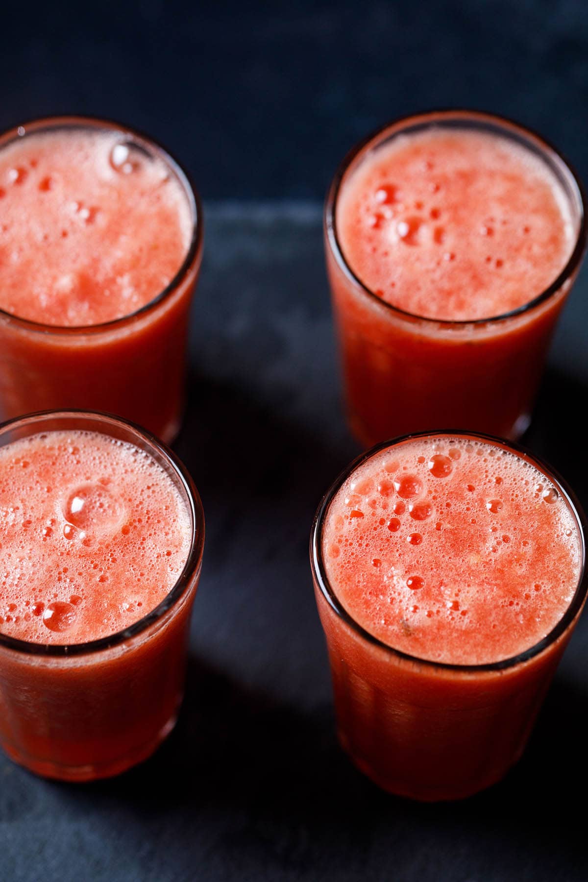 four tall clear glasses filled with watermelon juice on a black background