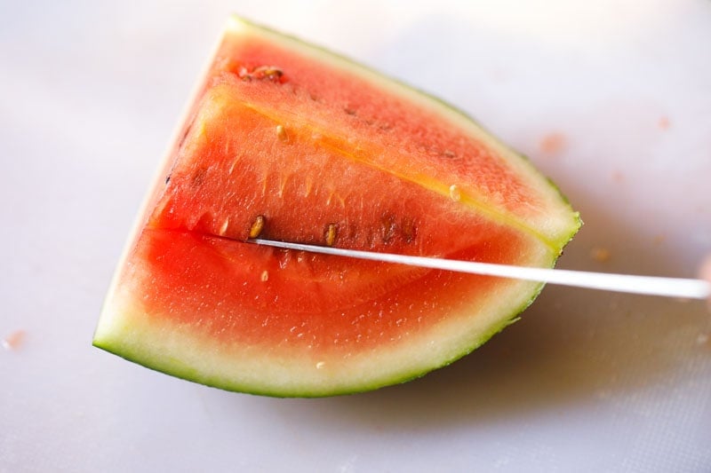 knife sliding under seed line of watermelon on first side