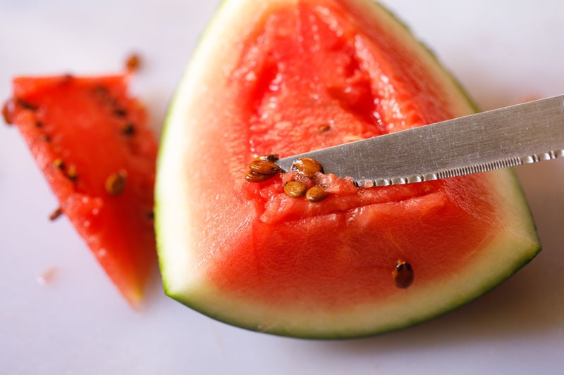 using knife to scrape seeds off larger piece of watermelon