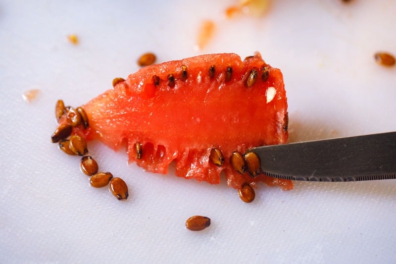 using knife to remove seeds on smaller, removed piece of melon
