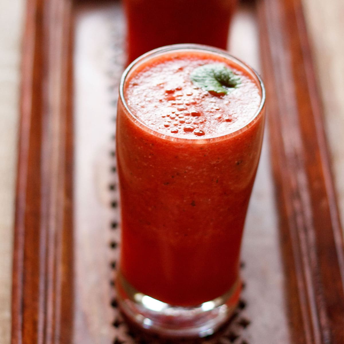 tall clear glass of watermelon mint juice topped with a sprig of fresh mint on a wooden serving tray