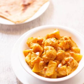 aloo gobi in a white bowl with paratha in another plate on a white board