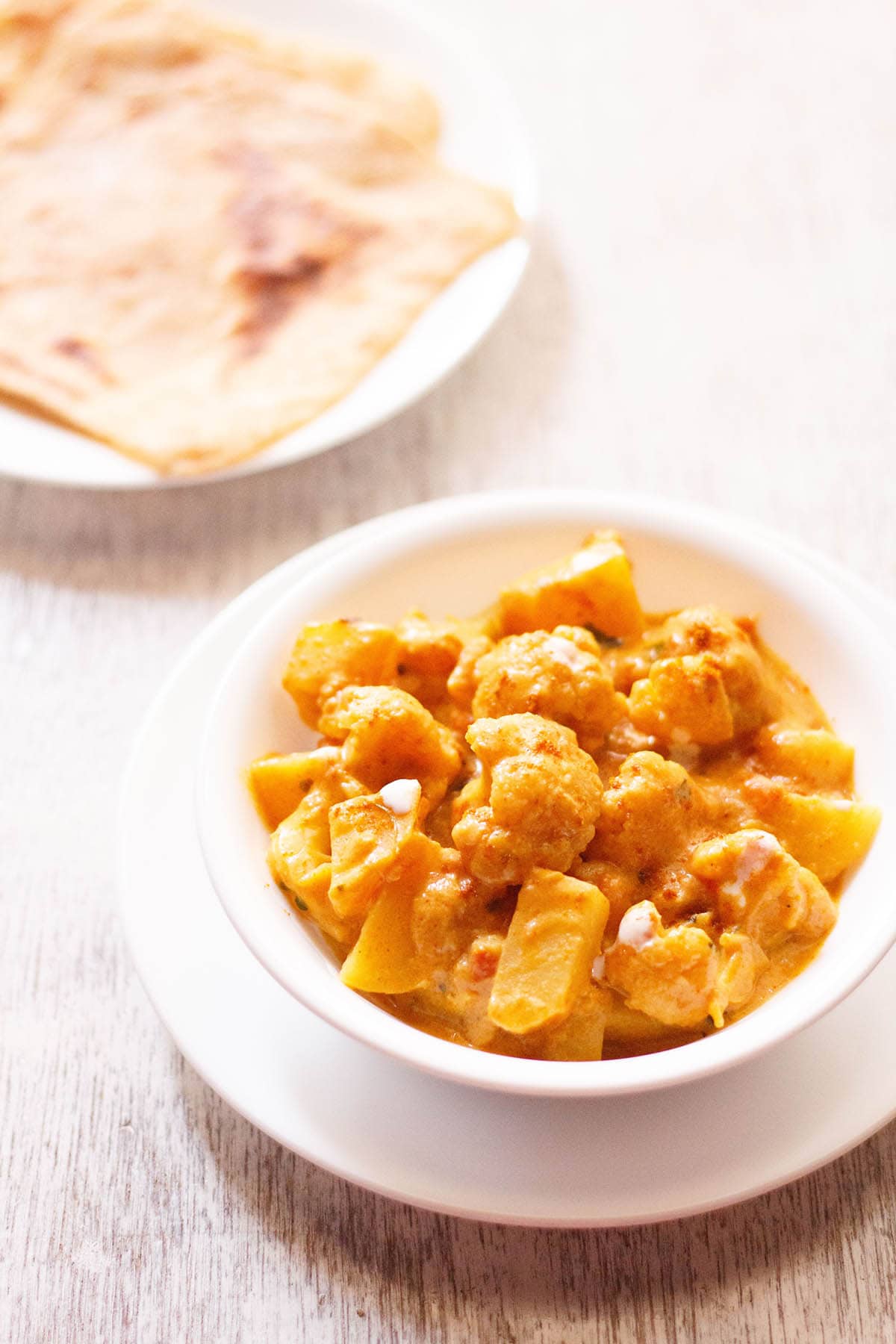 aloo gobi in a white bowl with paratha in another plate on a white board