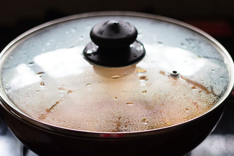 pan covered with a glass lid with simmering veggies inside