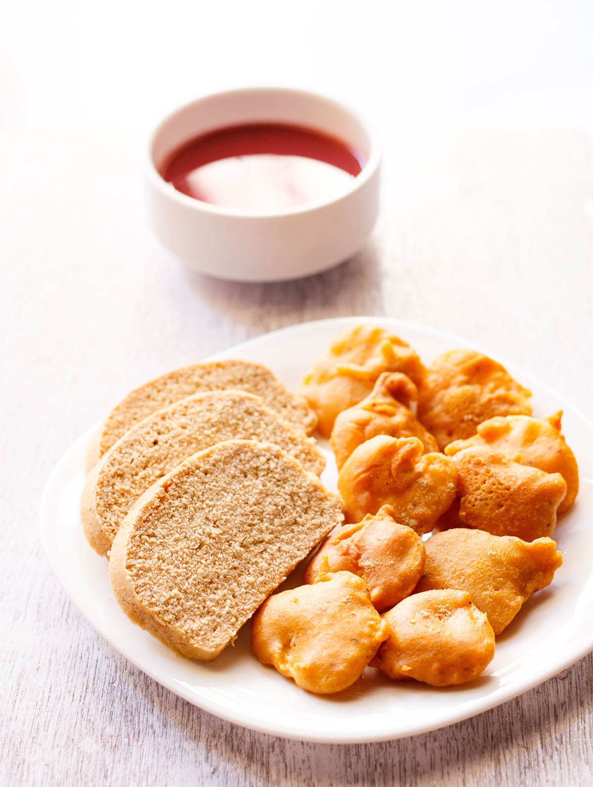 aloo pakora arranged on a plate with slices of wheat bread on a square plate