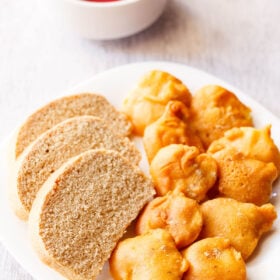 closeup shot of aloo pakora arranged on a plate with slices of wheat bread on a square white plate