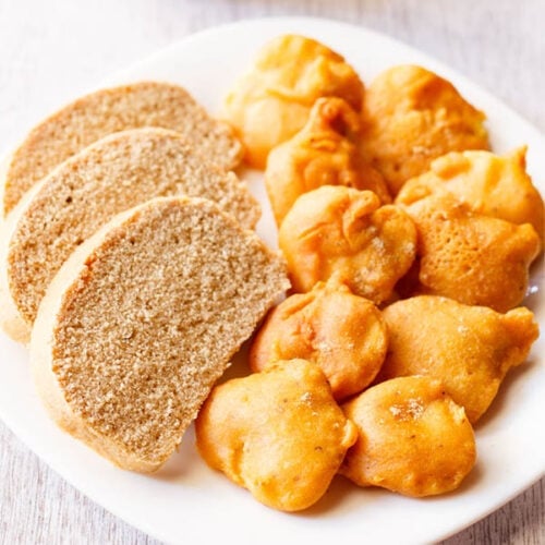 closeup shot of aloo pakora arranged on a plate with slices of wheat bread on a square white plate