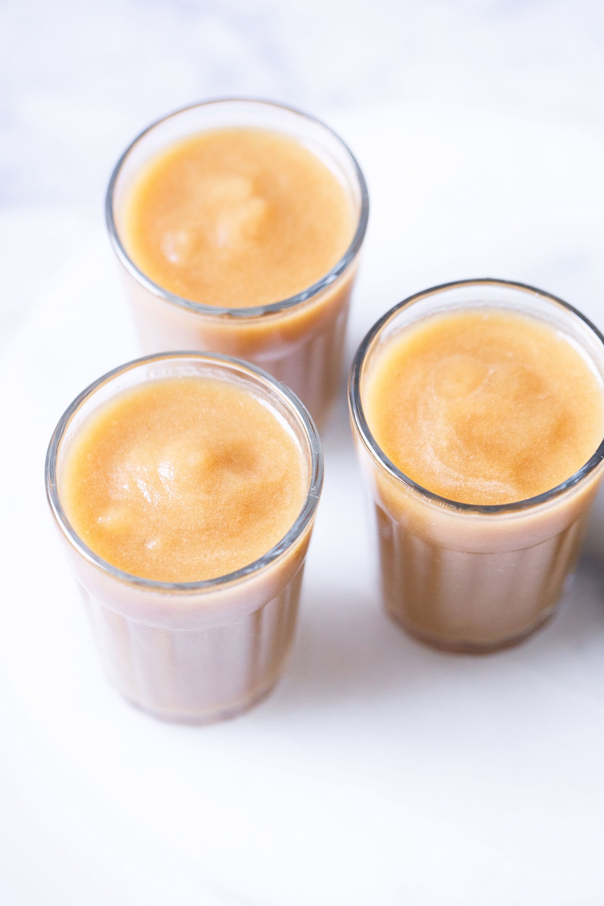 three clear glasses filled with homemade apple juice on a white table