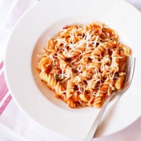 arrabiata pasta in a deep dish serving plate wit a silver fork by the side