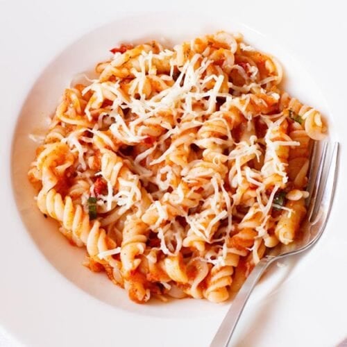 arrabiata pasta in a deep dish serving plate wit a silver fork by the side