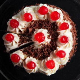 overhead shot of black forest cake on a black plate with a slice being removed