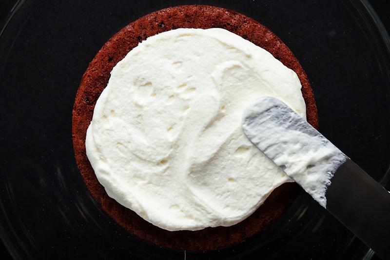 adding whipped cream on top of the first chocolate cake layer