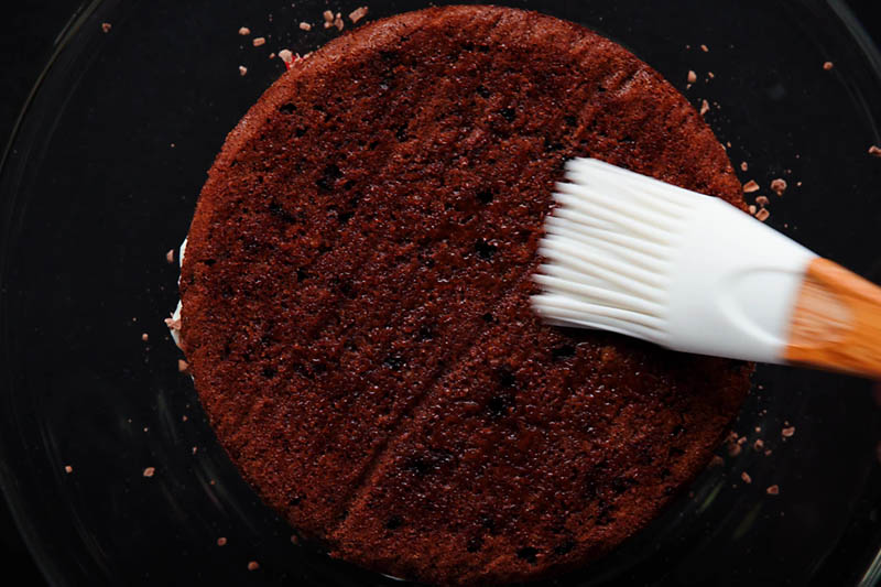 second layer of chocolate sponge being brushed with sugar syrup