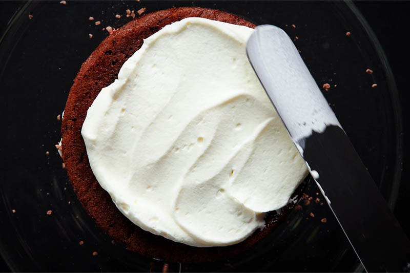 more whipped cream being added to the top layer with an offset spatula