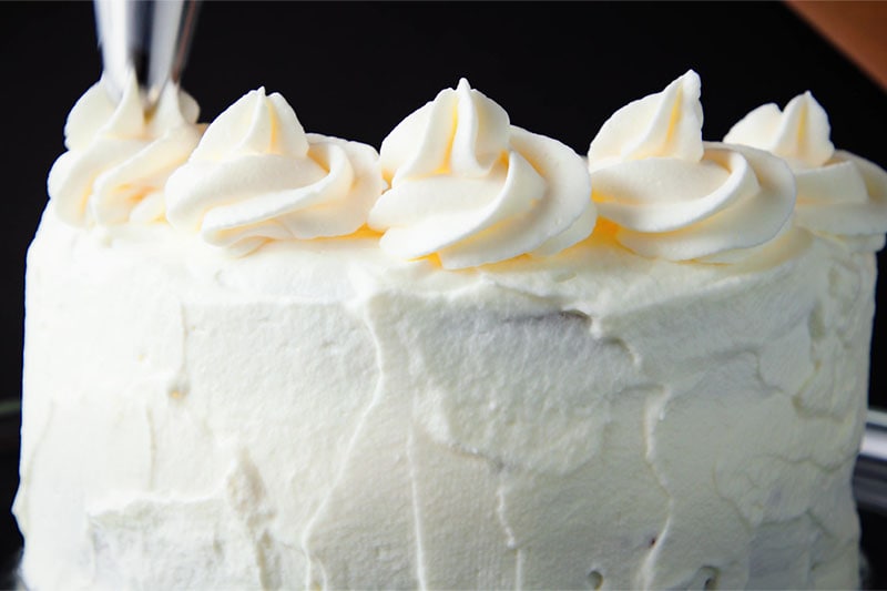 piping rosettes of whipped cream around the top of the frosted eggless black forest cake