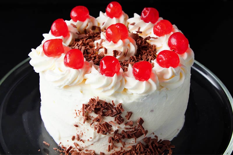 chocolate shavings being added to the side of the eggless black forest cake