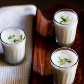 small three glasses filled with chaas placed on a wooden tray and a white linen