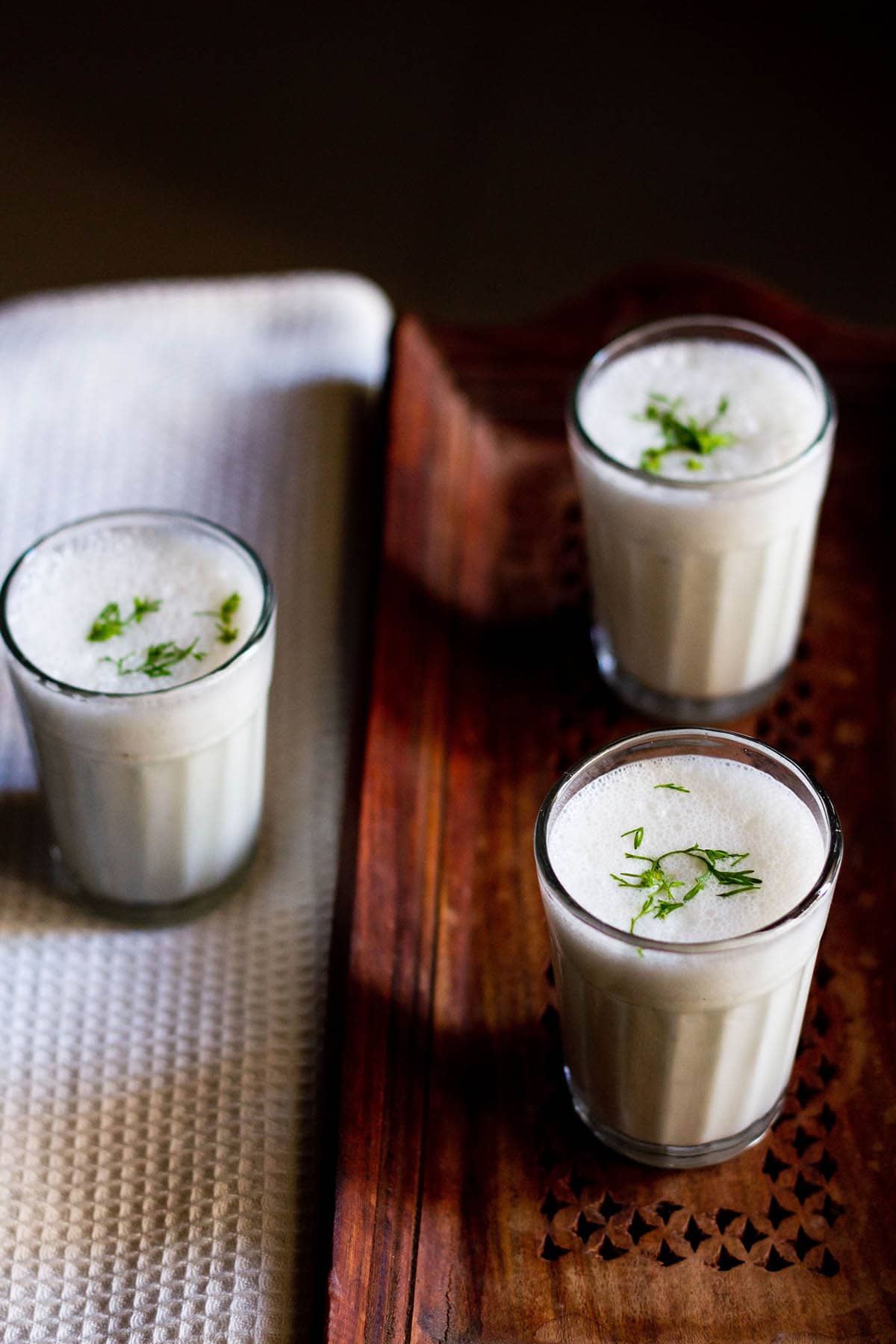 small three glasses filled with chaas placed on a wooden tray and a white linen