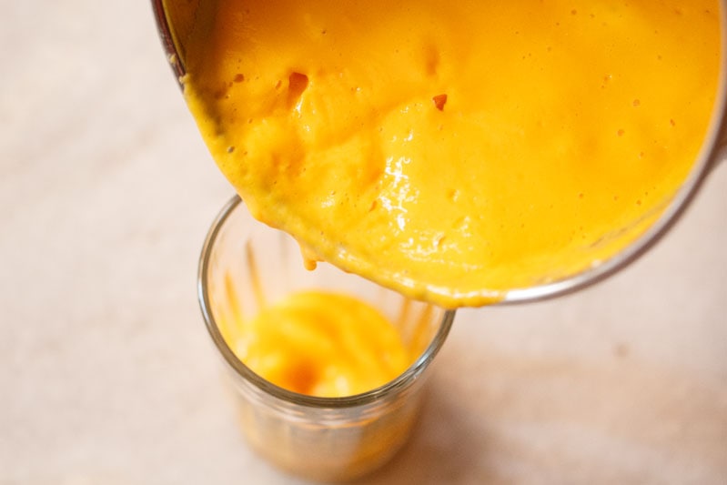 mango lassi being poured in a glass from the blender jar