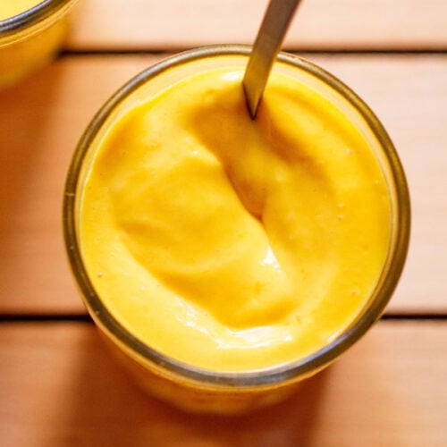 closeup shot of mango mousse in a small glass with a spoon inside