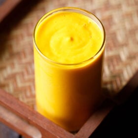mango smoothie in a glass on a matted wooden tray