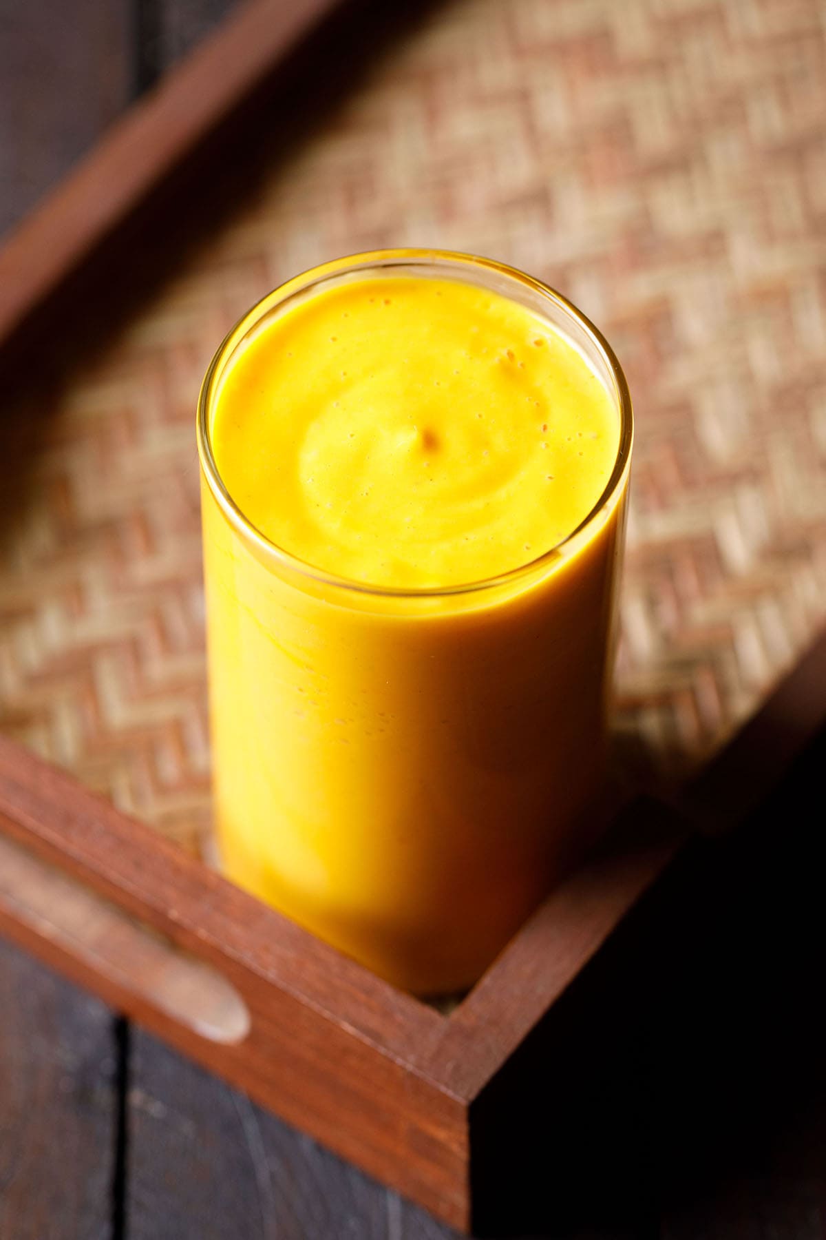 mango smoothie in a glass on a matted wooden tray