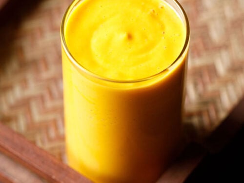 mango smoothie in a glass on a matted wooden tray
