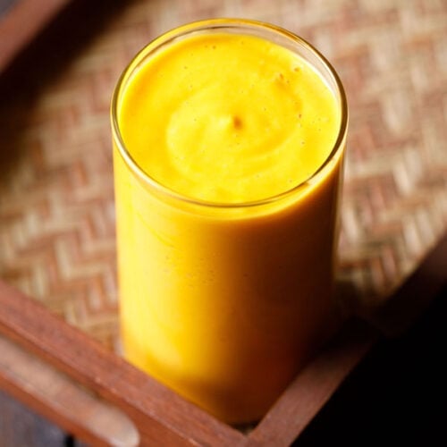 mango smoothie in a glass on a matted wooden tray