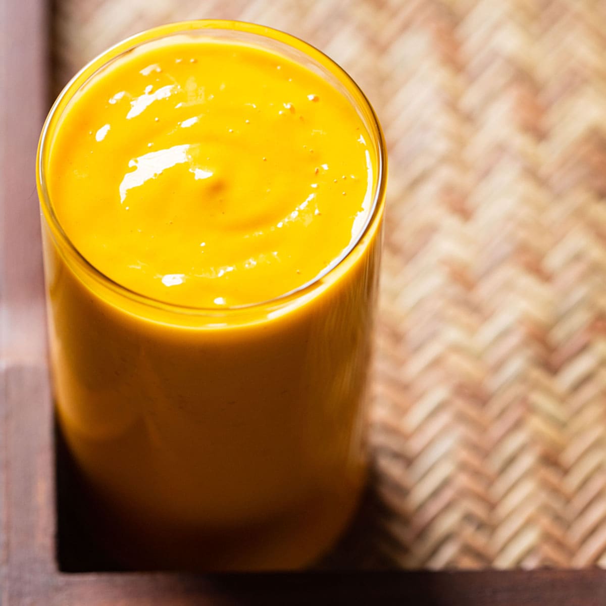 mango smoothie in a glass on a matted wooden tray