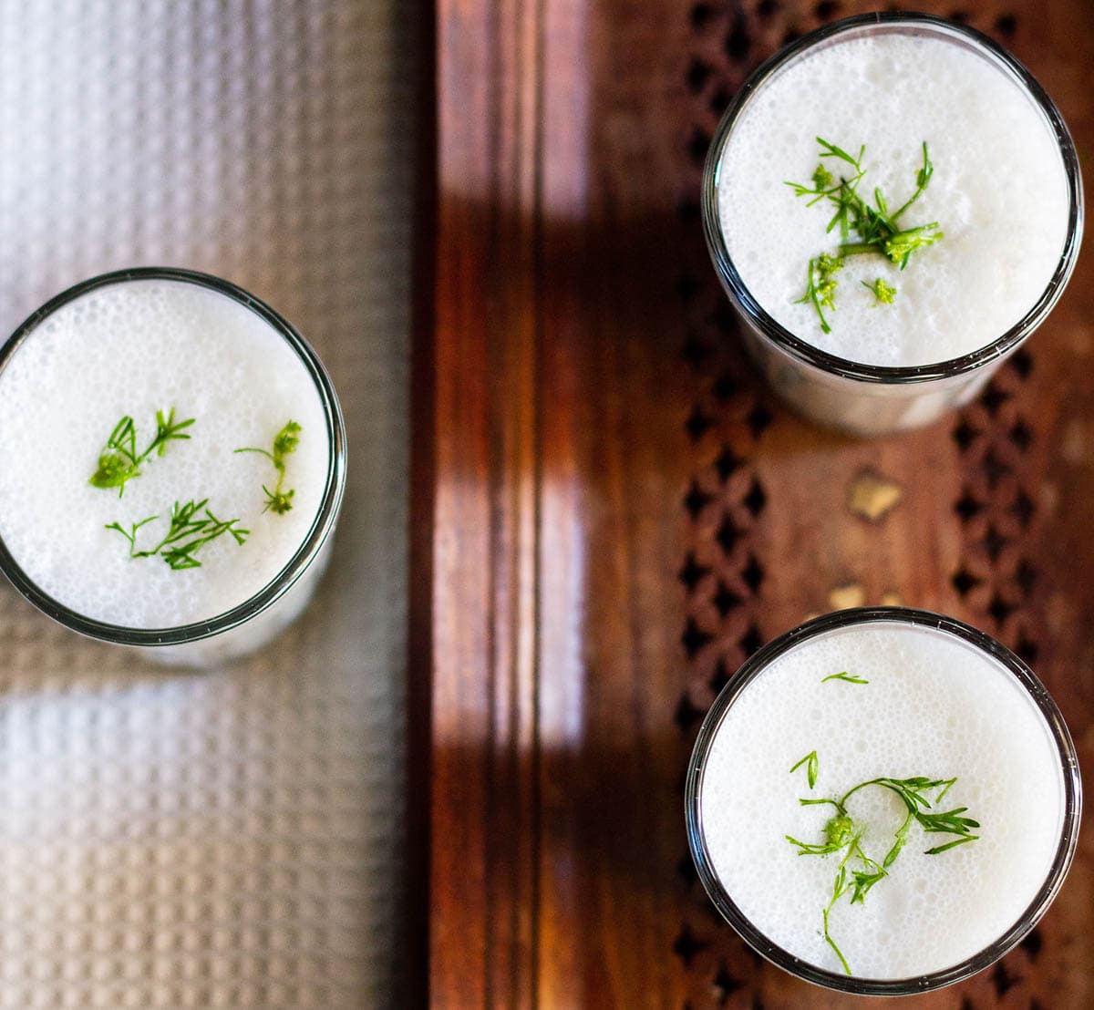 overheat shot of small three glasses filled with masala chaas placed on a wooden tray next to a white linen