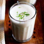 close up shot of masala chaas or chaas filled in a glass with a few cilantro sprigs