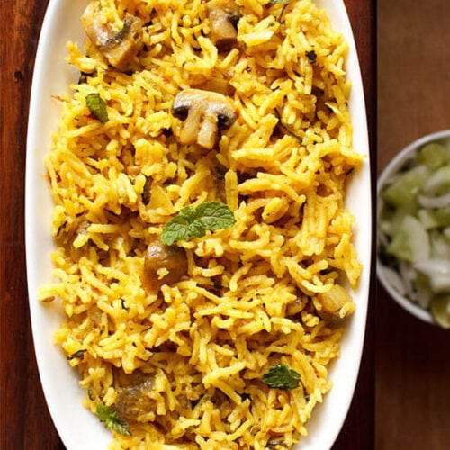 overhead shot of mushroom biryani in an oblong white tray on a wooden board