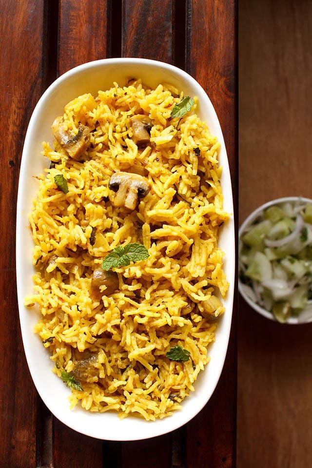 overhead shot of mushroom biryani in an oblong white tray on a wooden board