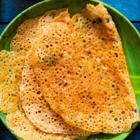 top shot of lacy crispy stacks of folded oats dosa on a green plate on a dark blue tray
