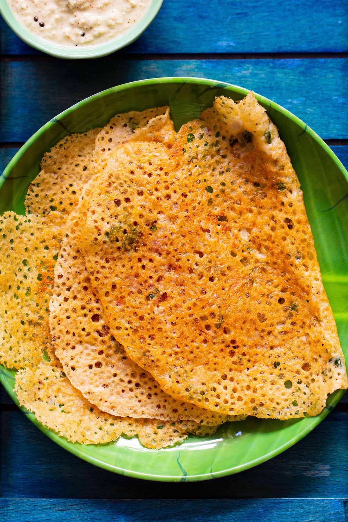 top shot of lacy crispy stacks of folded oats dosa on a green plate on a dark blue tray
