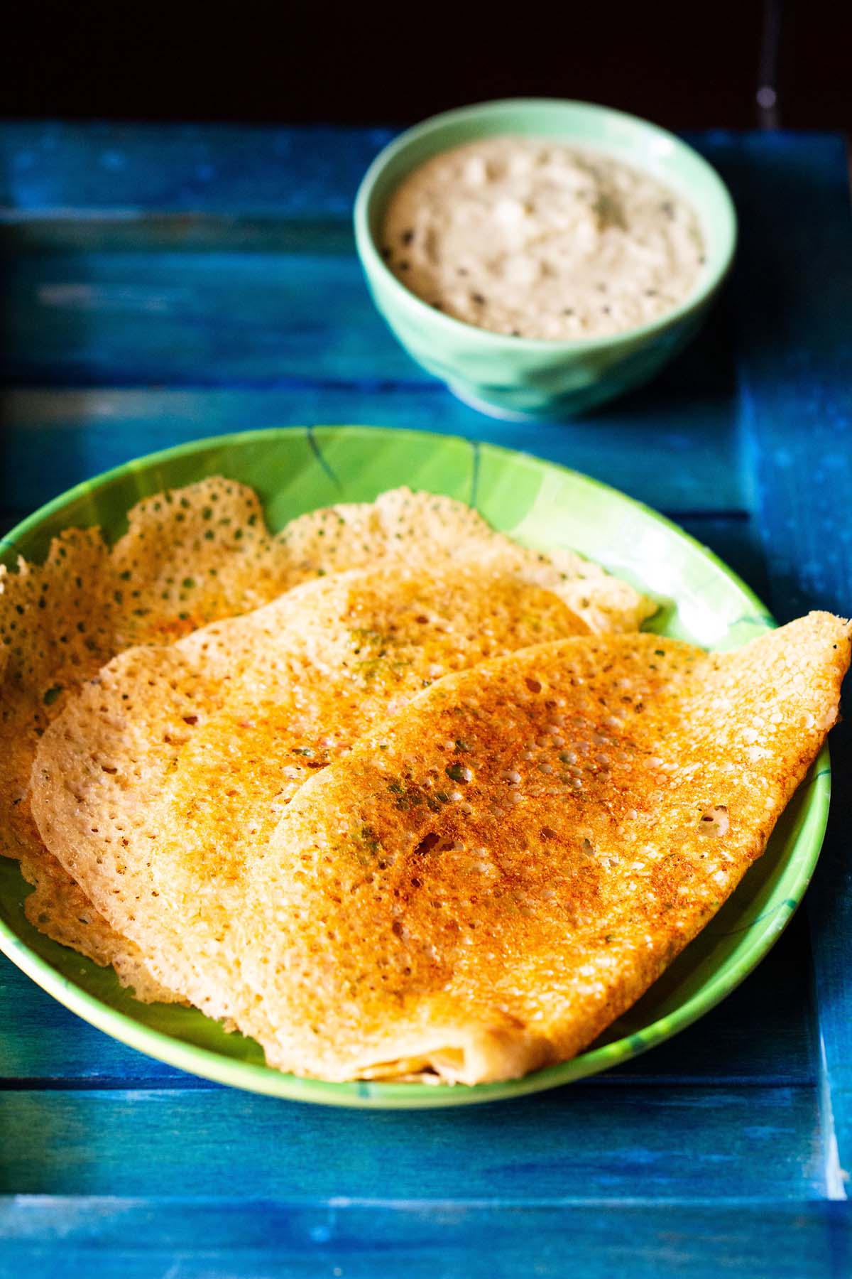 folded oats dosa placed on a green plate with a side of coconut chutney in a green bowl