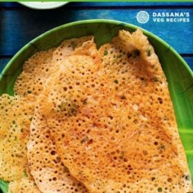 overhead shot crispy stacks of folded oats dosa on a green plate on a dark blue tray with text layover.