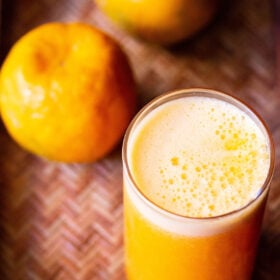 orange juice in a glass with two oranges on top on a cane tray