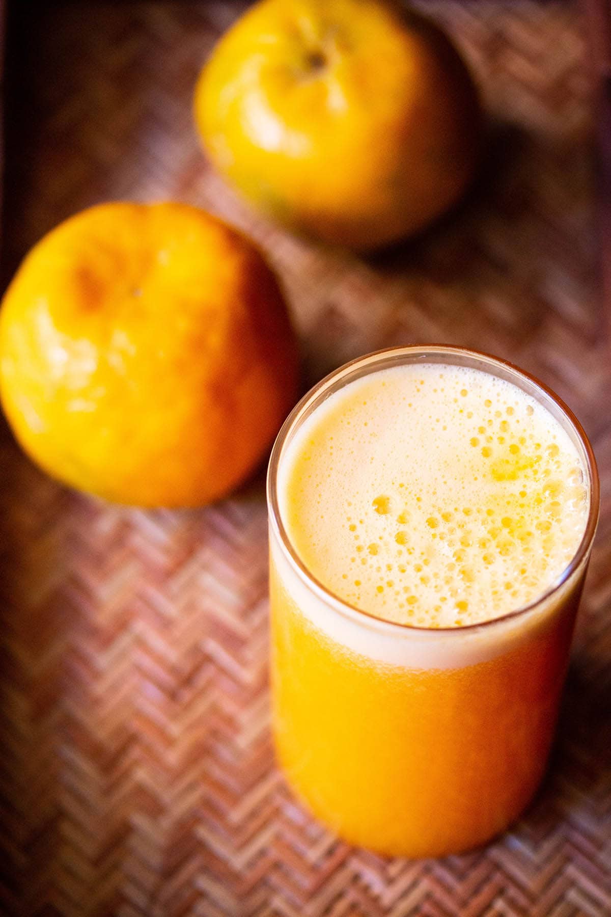 orange juice in a glass with two oranges on top on a cane tray