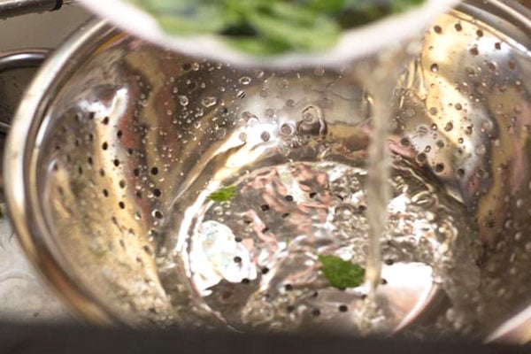 water from the methi leaves being poured in a steel colander