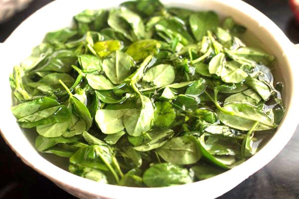 methi leaves soaking in water in a white bowl