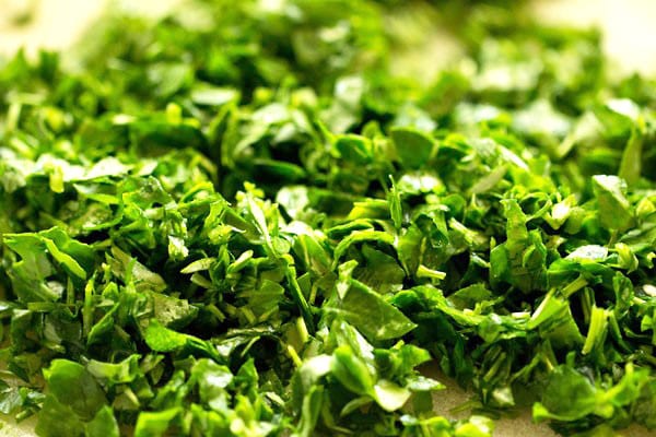 chopped methi leaves on a white chopping board